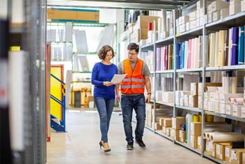 Man wearing safety jacket talking talking with women in warehouse