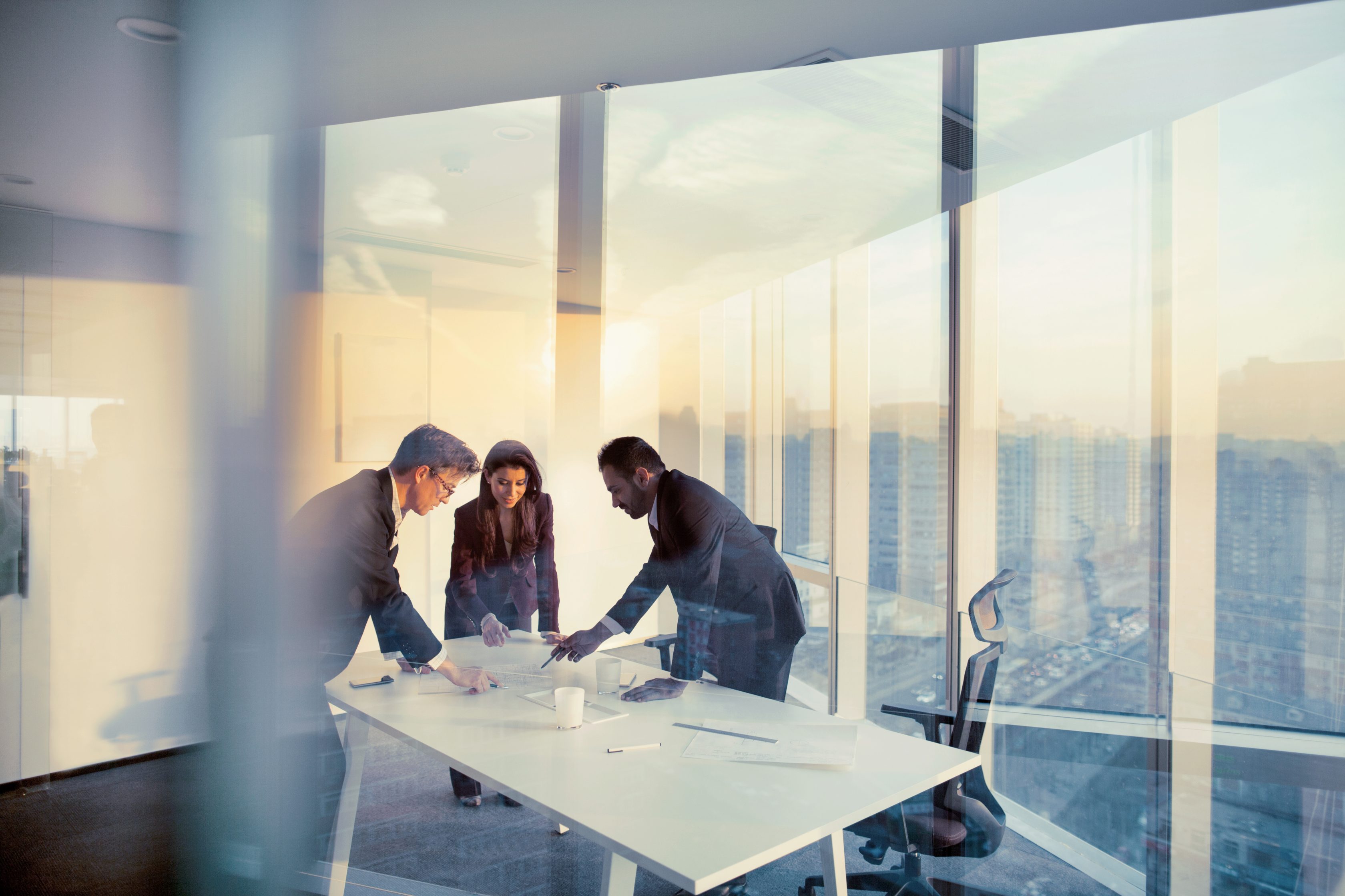 two men and a woman in office setting looking at laptop
