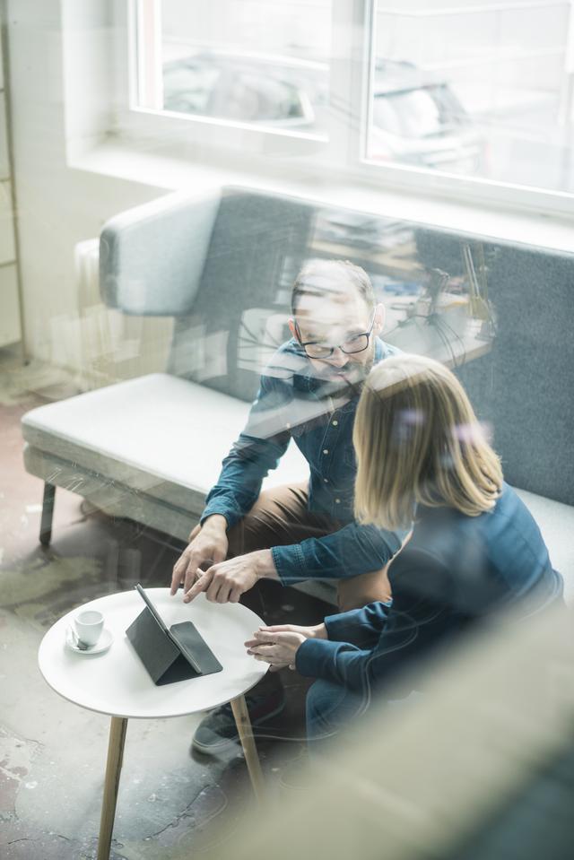 People talking, sitting in a couch and pointing to information on a computer