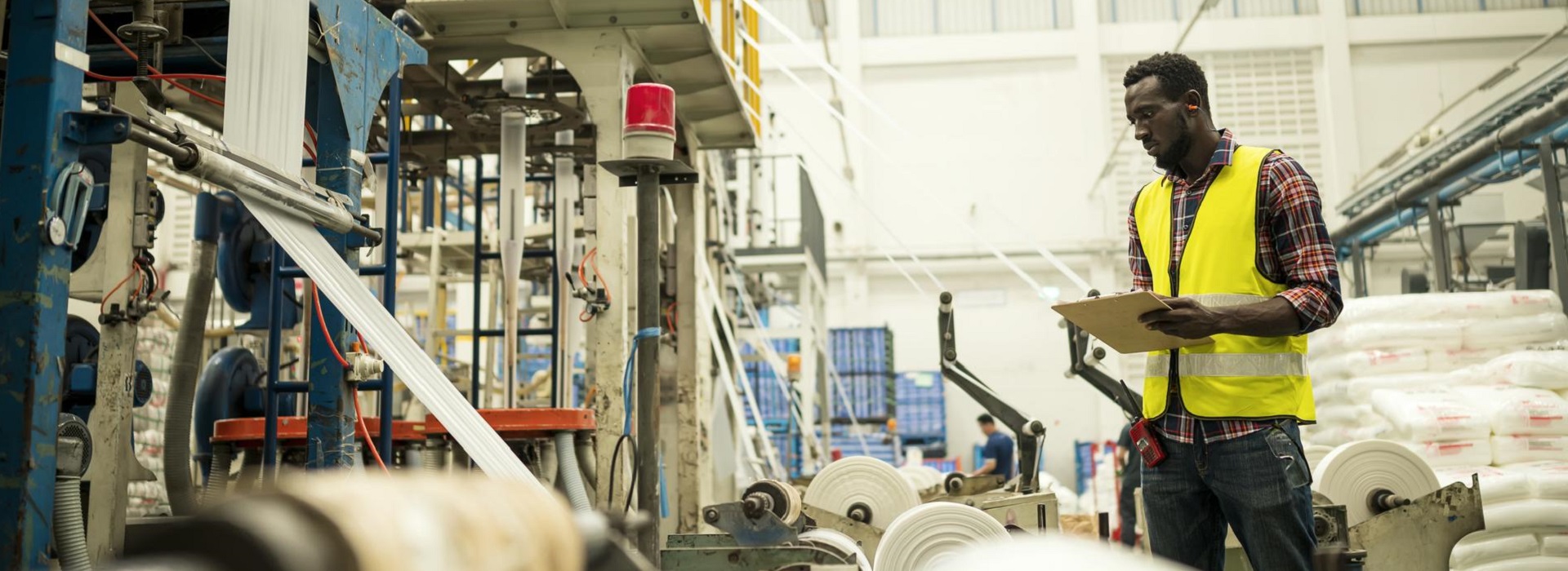 Un tecnico con gilet giallo controlla il funzionamento dei macchinari in un'industria cartaria