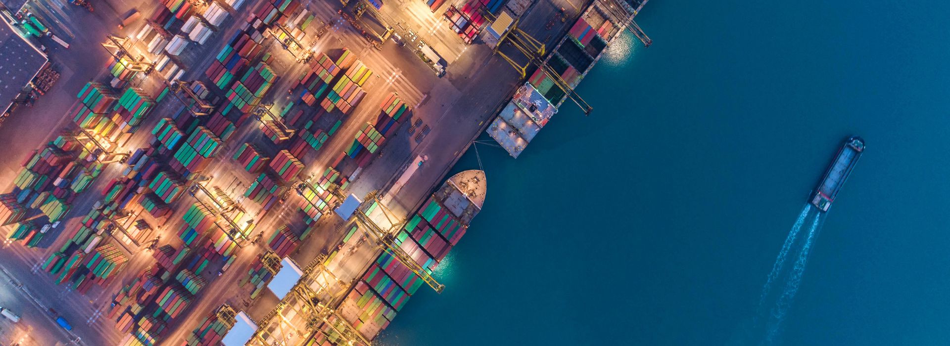 Molo di un porto commerciale visto dall'alto, con container destinati all'export e navi cargo