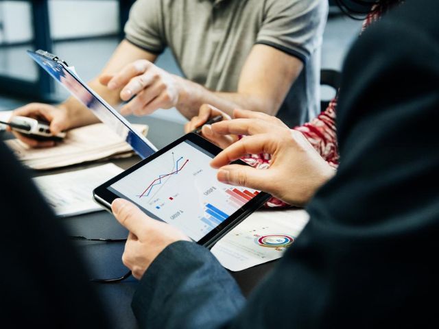 Dei colleghi consultano grafici su documenti e usando un tablet durante una riunione