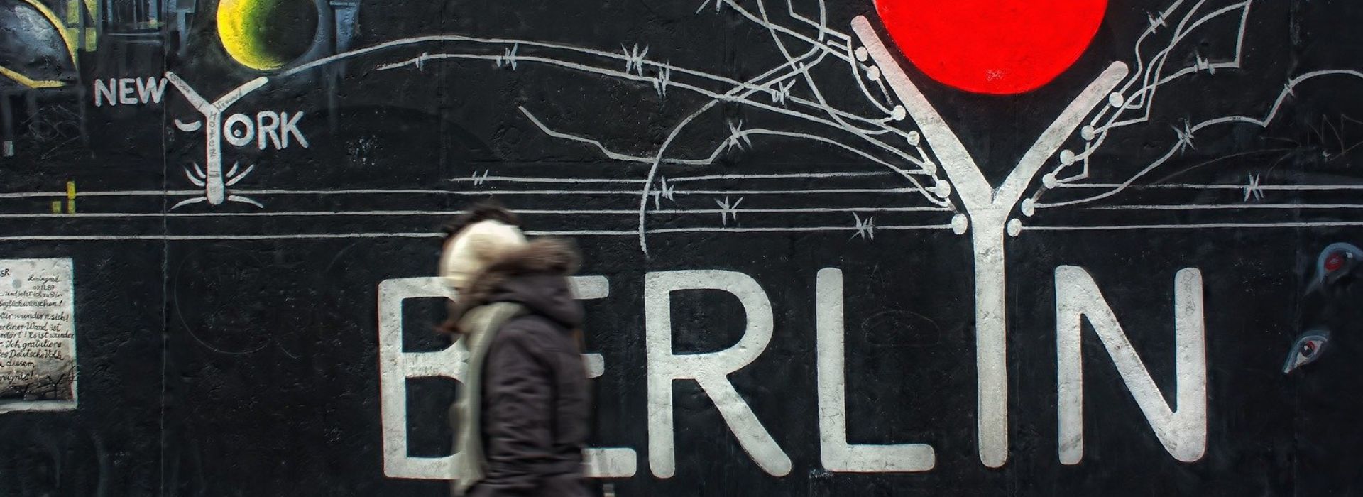 Una donna passa davanti ad un muro con street art a Berlino
