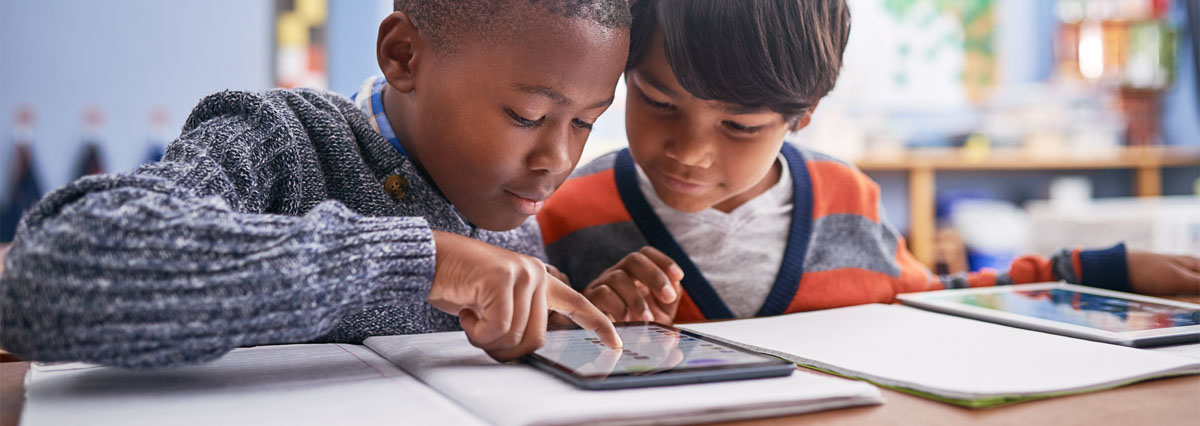 2 children in a classroom working with a tablet